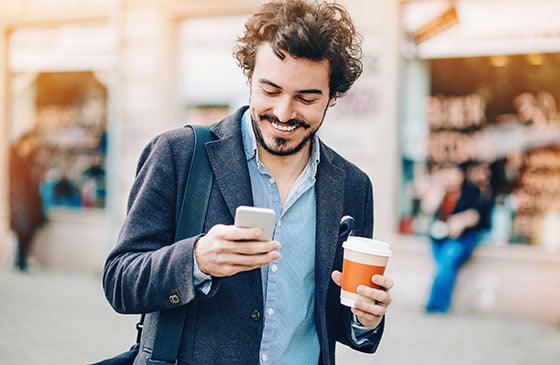 Man holding a cup of coffee scrolls through his cell phone.