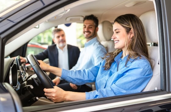 Mujer y hombre probando un coche con un representante de ventas fuera del coche.
