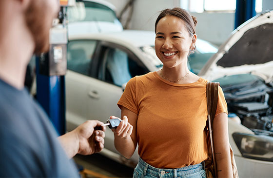 A young woman is given her keys back after repairs at a mechanic's shop.