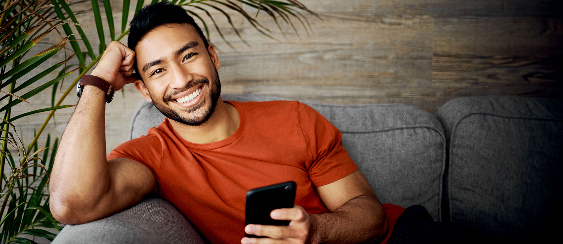 Man siting on couch smiling with phone in hand
