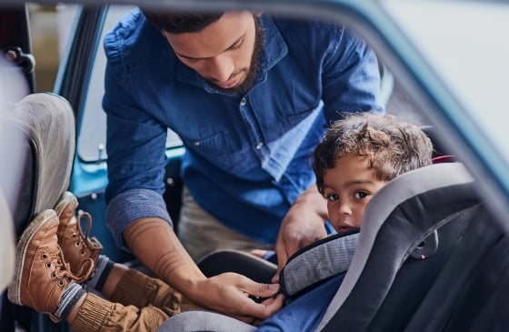 El padre abrochando el cinturón de seguridad del coche del hijo dentro del coche.