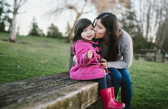 Women kissing child sitting on bench