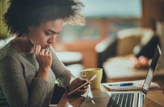 Women looking at her phone with laptop in front of her.