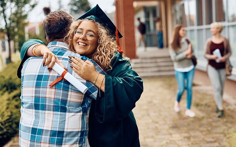 Graduating student in cap and gown hugging someone. 