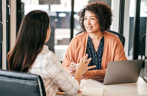 Two women sitting across from each other talking about business.