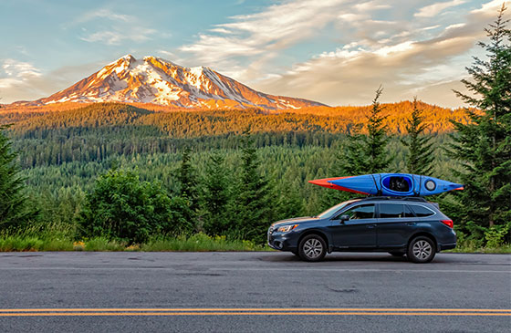Car with a kayak on its roof is parked along an interstate.