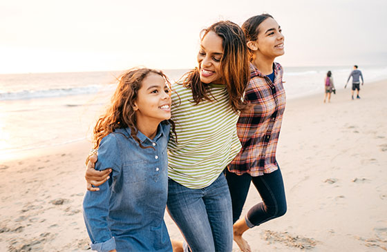 Woman and two daughters walk on a beach.