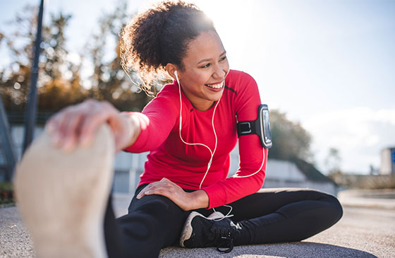 Women stretching leg while sitting on the ground listening to music