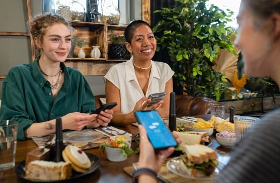 Friends out to eat and paying on their phones, sharing the bill.