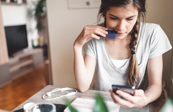 Younger unhappy lady looking at her phone and holding a credit card.