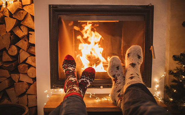 People wearing Christmas socks place their feet near a chimney. 