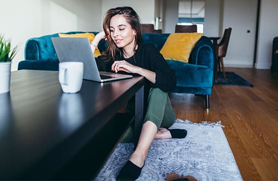 Girl sits on floor and scrolls through her computer.