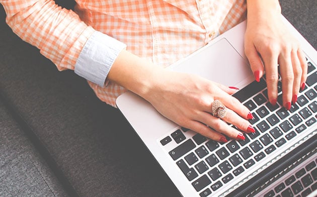 Woman in pink checkered shirt works on laptop.