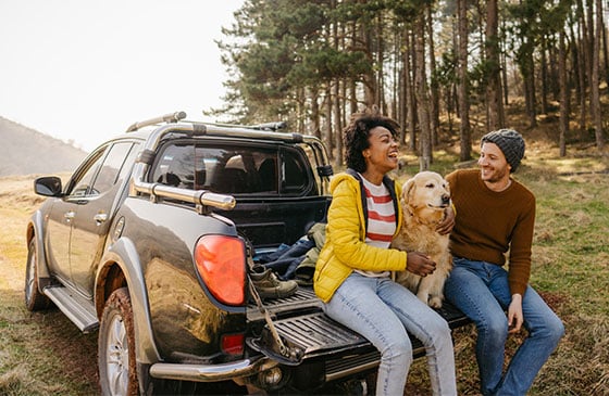 Couple with their dog sitting on a truck tailgate laughing.