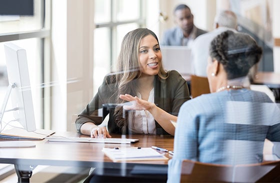Two people sitting at a desk talking about business