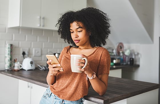 Woman sitting in her kitchen looking at her phone.