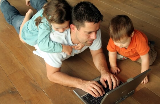 Dad with little kids on the floor with laptop.