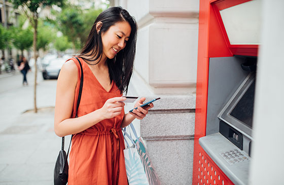 Younger women accessing money from phone near ATM