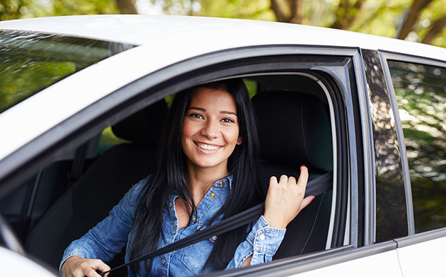 Young woman smiles as she puts her seat belt on. 
