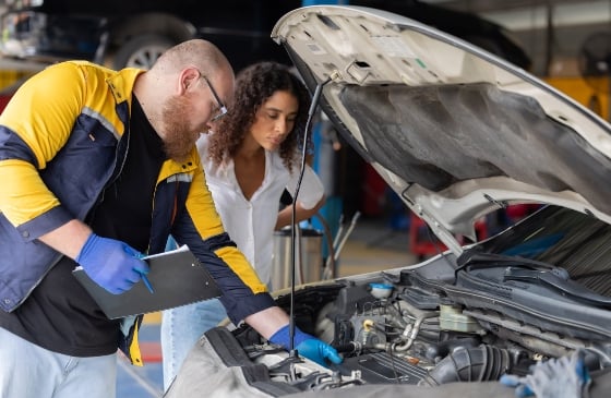 Mecánico mirando un motor de coche con el capó abierto.