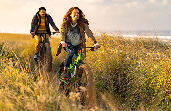 Man and woman ride bikes through a field.