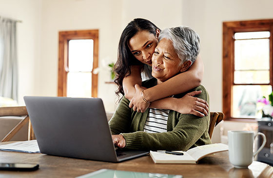 Woman on laptop while daughter is hugging her
