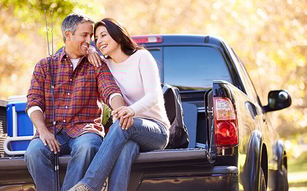 Man and woman sit on the bed of their truck. 