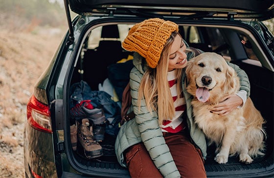 Woman sits with her dog on the truck of her car.